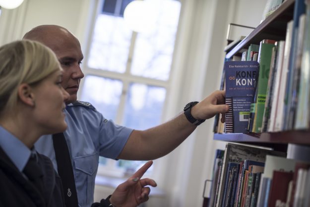 To fængselsbetjentelever i uddannelsescenteret i Birkerøds bibliotek. Den ene elev tager en bog ned fra reolen, som den anden peger på.